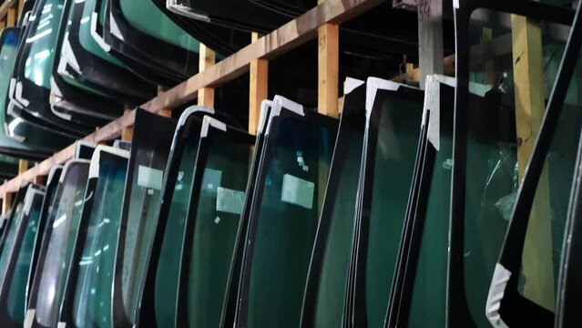 Lots of windshields for different cars on service station shelves ready to install or replace broken glass with cars.