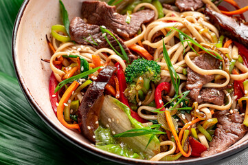 Udon stir fry noodles with beef meat and vegetables in a plate on white wooden background.
