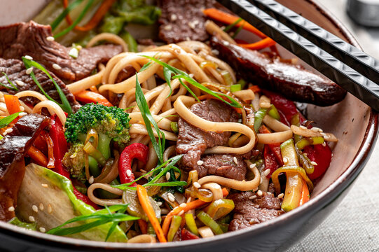 Udon stir fry noodles with beef meat and vegetables in a plate on white wooden background.