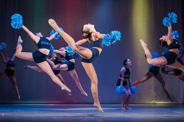 athletes perform on stage, young cheerleaders perform at the cheerleading championship, girls in a jump, girls are holding pompons, hands raised up, girls dancer practicing mixed dance and stretching