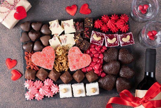 Charcuterie sweet board with different sweets, chocolate, marmalade hearts, nuts and candies as well wine and two glass on brown background. Snacks dessert for romantic Valentines Day, Top view