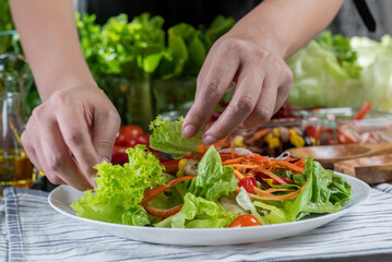 woman chef mix fresh baby cos salad and pour salad dressing in glass blow. Organic Vegetables mix all green salad In glass bowl. Breakfast fresh salad and clean vegetable.