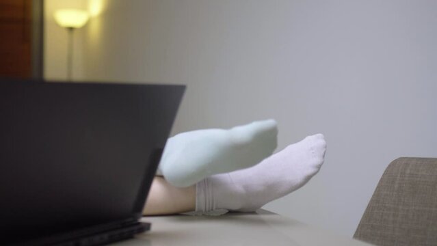 Girl at home living room with feet on a table infront of a laptop computer. Student with different color socks taking online course. Home education concept.