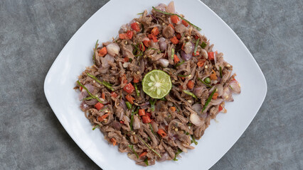 Soft focus chicken or beef with traditional Indonesian sambal. Onions, chilies, coconut oil, lime leaves, salt. Served on a white plate and stone plinth.