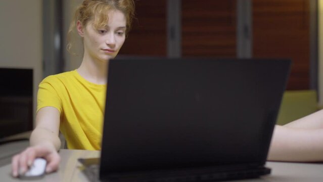 Serious girl working on a laptop at home. Casual clothing with feet wearing different color socks up on the table in a living room. Portrait of a student taking online course. Home education.