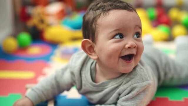 Adorable hispanic baby holding xylophone lying on floor at kindergarten