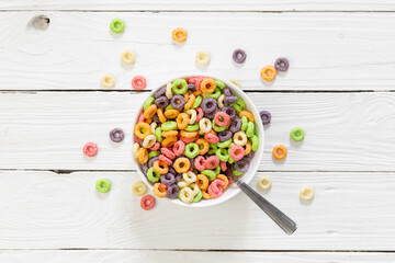 Naklejka na ściany i meble Colored breakfast cereals laid out in a bowl on a white wooden background, top view, children's healthy breakfast.