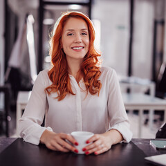 Portrait of a young business woman drinking coffee at the desk in the office.