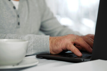 Closeup of senior man hands using laptop. Cropped side view of wrinkled caucasian older hands typing keyboard. Old people with technology. Unrecognizable retired male working from home sitting at desk
