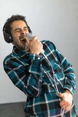 Mixed race man dressed in checked shirt singing into a condenser microphone