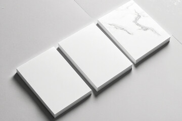 Three empty white rectangle poster mockups are close ups that are arranged diagonally on a light grey concrete background. Top view of a flat lay. Open structure. Generative AI