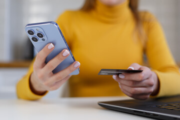 Young woman makes a purchase online with a credit card and smart phone. Close up photo of female hands holding modern mobile phone and plastic bank card for payment