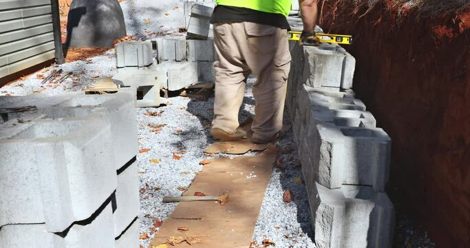 On construction site of construction worker was installing concrete block for retaining wall next to new house