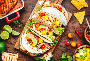 Tacos with grilled chicken, tomato salsa sauce, mango, cilantro and onion in corn tortilla on wooden board. Rustic table background, top view - obrazy, fototapety, plakaty