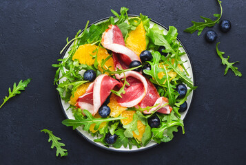Delicious salad with smoked duck, oranges, blueberries, arugula and lettuce, black table background, top view