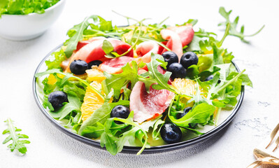 Gourmet salad with smoked duck, oranges, blueberries, arugula and lettuce, white table background, top view