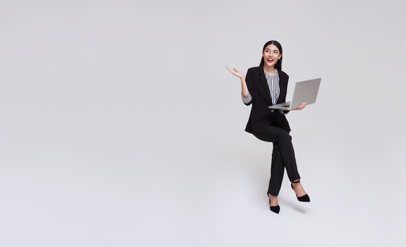 Young business woman asian happy smiling. While her using laptop sitting on white chair and looking isolate on copy space studio background.