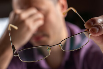 Tired young man feel pain eye strain holding glasses rubbing dry irritated eyes fatigued from computer work,