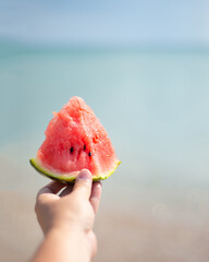 Watermelon slice in hand. Beach and sea. Ocean coast. Picnic on the coast. Vegetarian food in nature