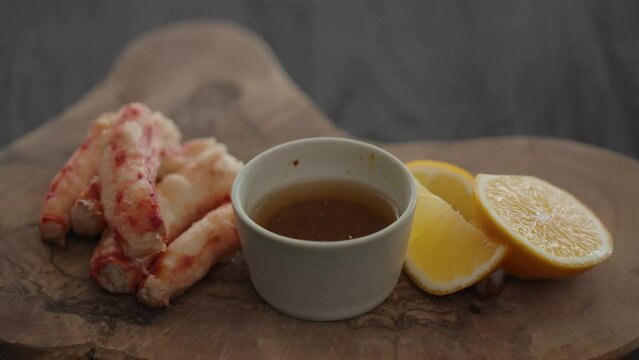 Slow motion gimbal shot of crab leg meat on a olive board with sweet lemon and dip sauce