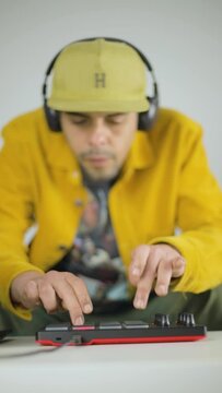Mixed race man making beats from his sofa at the coffee table with an MPD MIDI controller. Vertical video