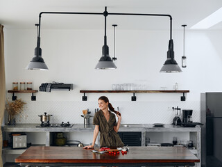Happy woman chef stands in Stylish minimalist kitchen interior with natural elements in wood and stone design with fresh produce for dinner on the table, copy place, homemade food in a clean room