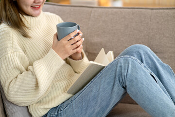 Obraz premium young asian woman holding a cup of coffee and a book on the cozy sofa