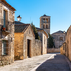 Street of beautiful medieval buildings with church tower in the background in the monumental city of Pedraza, Segovia, Spain.