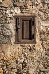 Small wooden window recessed in a medieval stone building in the monumental town of Pedraza, Segovia.