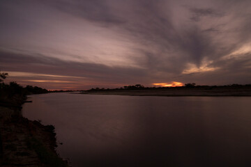 Long exposure shot of Corriente river  in Esquina, Corrientes, Argentina, at sunset. Beautiful blurred water effect, dramatic clouds and hiding sun at nightfall.  