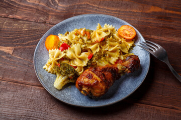 Pasta with vegetables and cherry tomatoes with baked chicken leg on the table