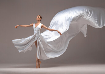 Ballerina in white ballet dress danсing on pointe shoes in white studio.