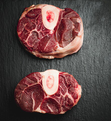 
cut of osso buco meat, on marble slate table black background, raw piece, without people, vertical, with copy space