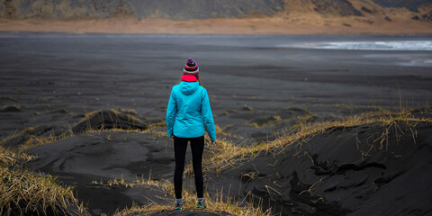Girl in a blue jacket walking on famous black sand beach Vestrahorn admiring atlantic ocean, Iceland