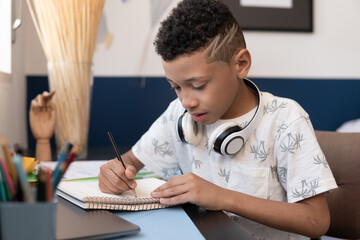 Young boy writes in school notebook at table in room