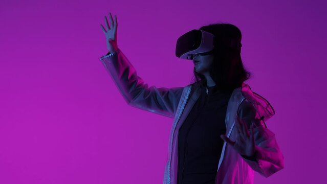Woman in futuristic costume. Female in modern VR glasses interacting with network while having virtual reality experience. Augmented reality game, future technology, AI concept. VR. Neon light.