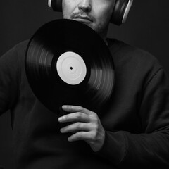Lifestyle and hobby concept. Man with sweatshirt and headphones on his head abstract studio portrait. Model holding blank LP vinyl record near face. Black and white image