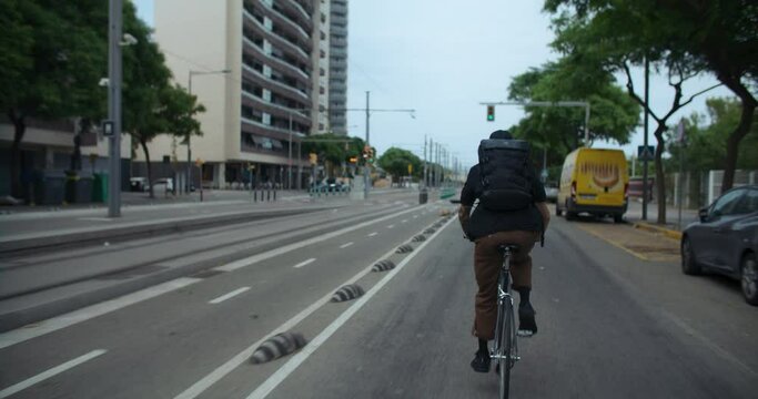 Follow shot of young man ride bike in city, on bike lane. Urban city planning infrastructure for cyclists. Speeding up to arrive in time. Eco friendly and efficient transportation choice