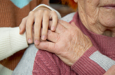 The hands of an old and a young woman embrace each other. Love and care for the older generation,...