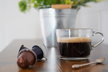 Cup of black coffee next to some capsules