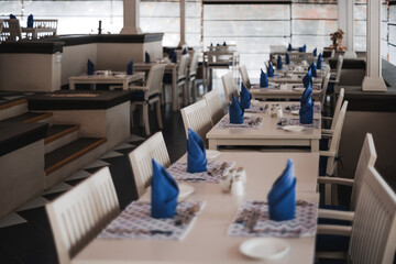 Selective focus on white wooden tables and chairs, in a restaurant on the pacific island. The dinner tables are dressed with crisp blue napkins and neatly disposed of silverware.