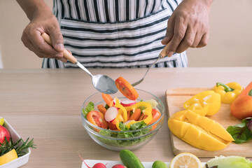 The concept of a healthy diet and lifestyle. Man is preparing a salad of various vegetables in the kitchen.