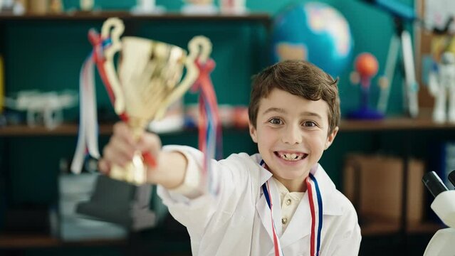 Adorable hispanic boy student smiling confident holding trophy at laboratory classroom