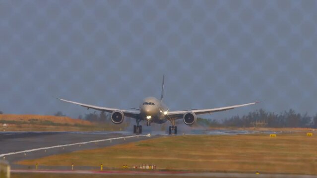 Wide body airliner landing and touching on the runway at Phuket airport. View through the fence. Airplane on the airfield. Travel concept