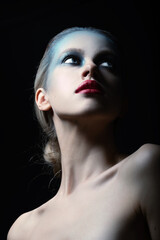 Fototapeta premium Fashion concept. Studio portrait of beautiful woman with fancy and futuristic blue, gray make-up and red lipstick. Model with blue eyes looking up and aside camera. Toned image with dark blue color