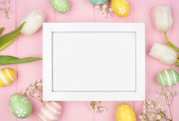 White wood frame with pastel Easter eggs and white spring tulip flowers. Above view against a pink...