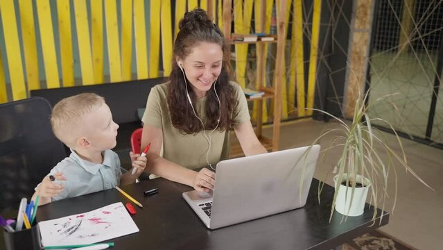 Mother listening to music using laptop, curious kid nearby