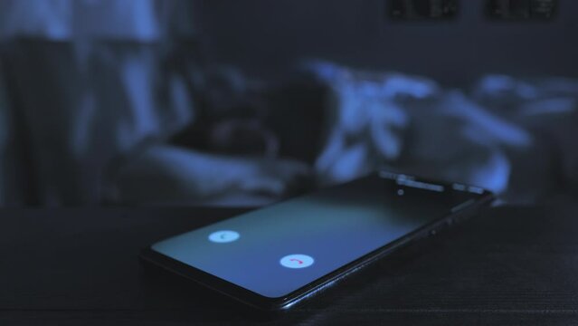 infidelity love affair,close up on mobile phone receiving incoming call while a married couple sleep on bed in the background,betrays cheating concept