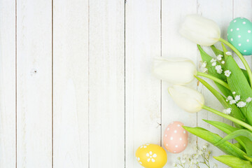 Pastel Easter eggs and white spring tulip flowers. Top view side border against a white wood background. Copy space.