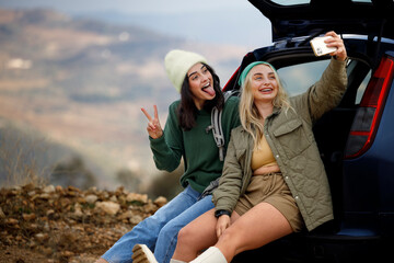 Happy female friends taking a selfie in the back door of a car with a rural landscape in the background